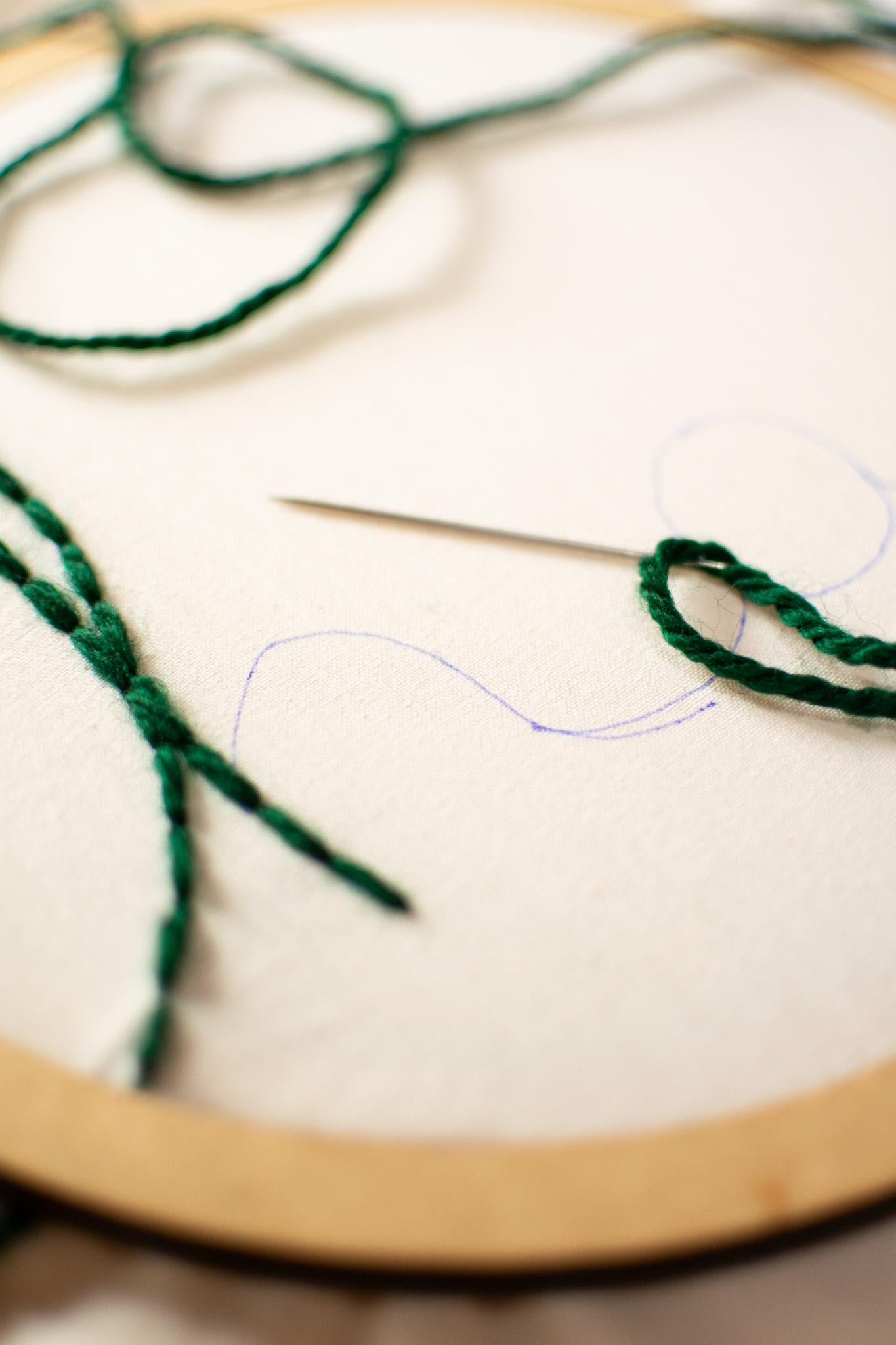 Embroidery hoop with green thread and needle on a white fabric background